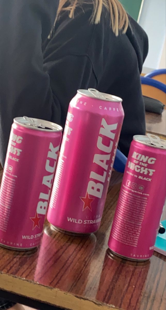 three cans of black cherry soda sitting on a table next to a woman's laptop