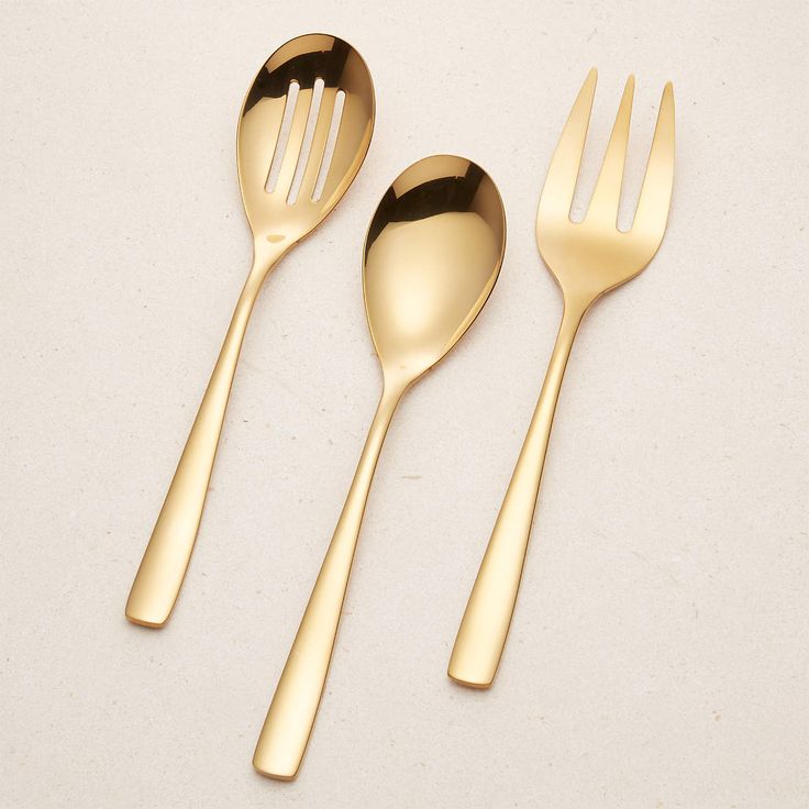 three golden spoons and two forks on a white surface