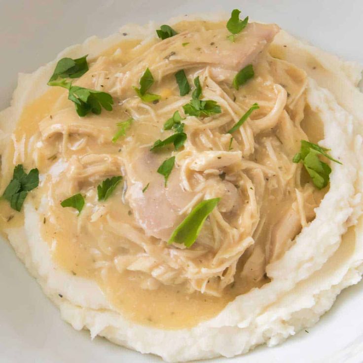 chicken and gravy on top of mashed potatoes in a white bowl with green garnishes