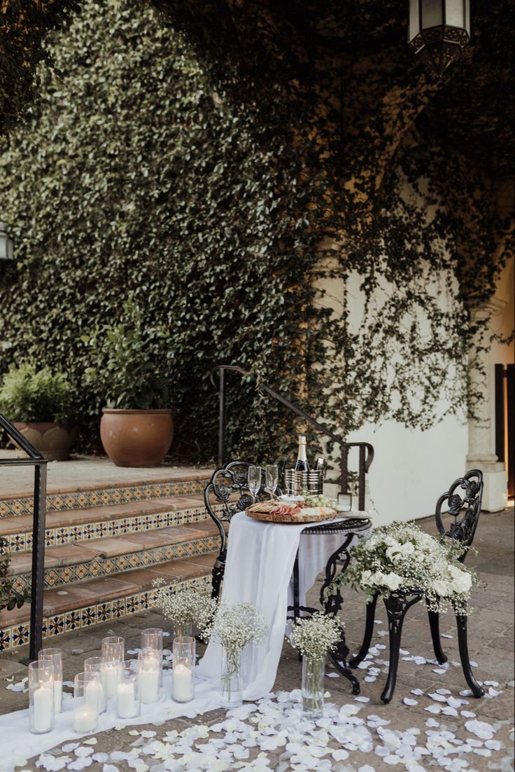 an outdoor table with candles and flowers on the ground next to some stairs in front of a building