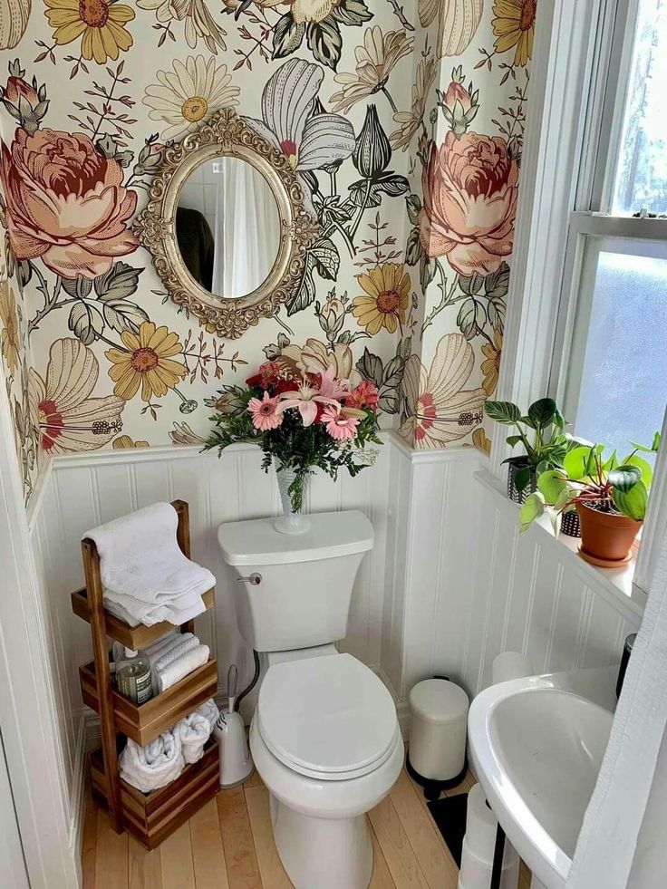 a white toilet sitting in a bathroom next to a sink under a mirror and flowered wall paper