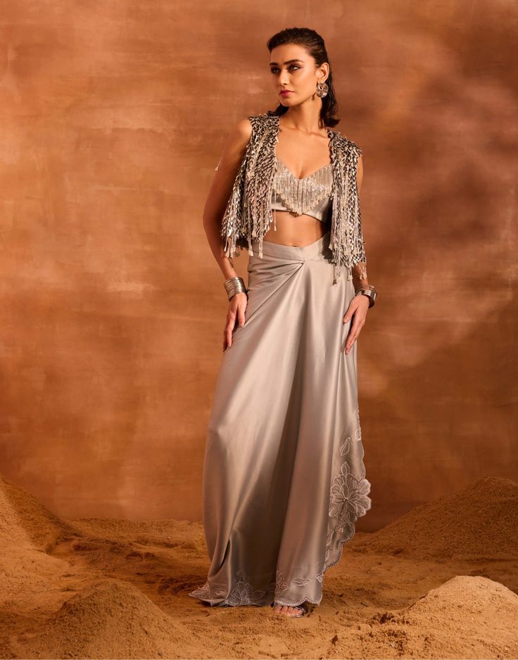 Adorned with hand-embellishments, blaze jacket set features a tassel-embellished blouse paired with a flowing satin draped skirt. The jacket's feather-like details add a luxurious flair, making it a standout ensemble. Elegant Party Pre-draped Saree With Tassels, Glamorous Draped Sets With Sequins, Elegant Draped Sequin Lehenga, Glamorous Draped Sequin Sets, Elegant Draped Sets With Sequins, Elegant Pre-draped Sequin Saree For Gala, Elegant Draped Sequin Sets, Elegant Pre-draped Saree With Sequins For Gala, Silk Floor-length Sets With Draped Sleeves