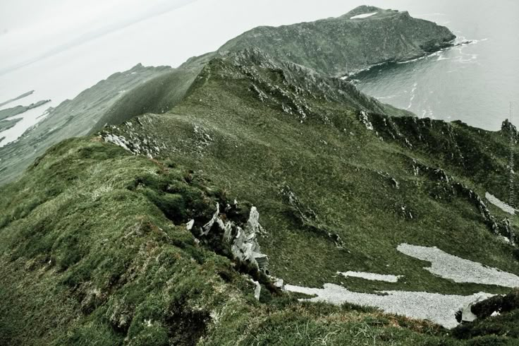 the top of a grassy mountain with water in the background