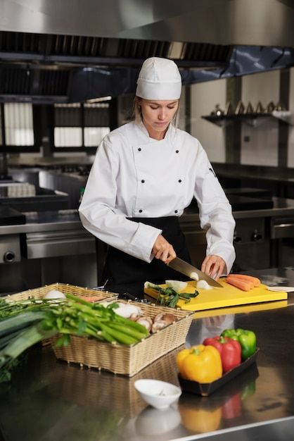 a woman in a chef's outfit cutting vegetables on a counter top with a knife