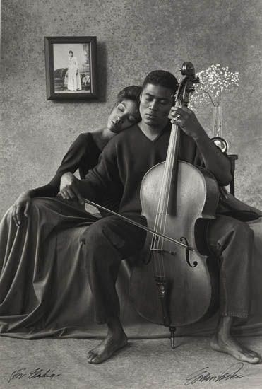 a man and woman sitting on a couch with a cello in front of their faces