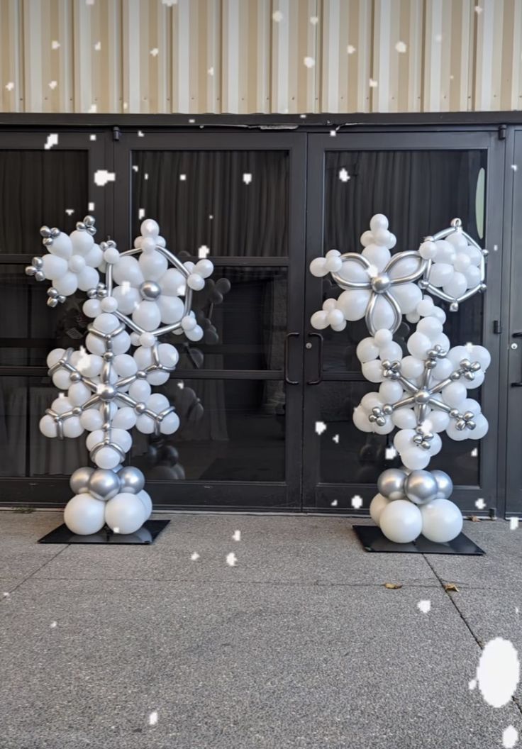 two large white balloons are in the shape of snowflakes on black stands with silver balls