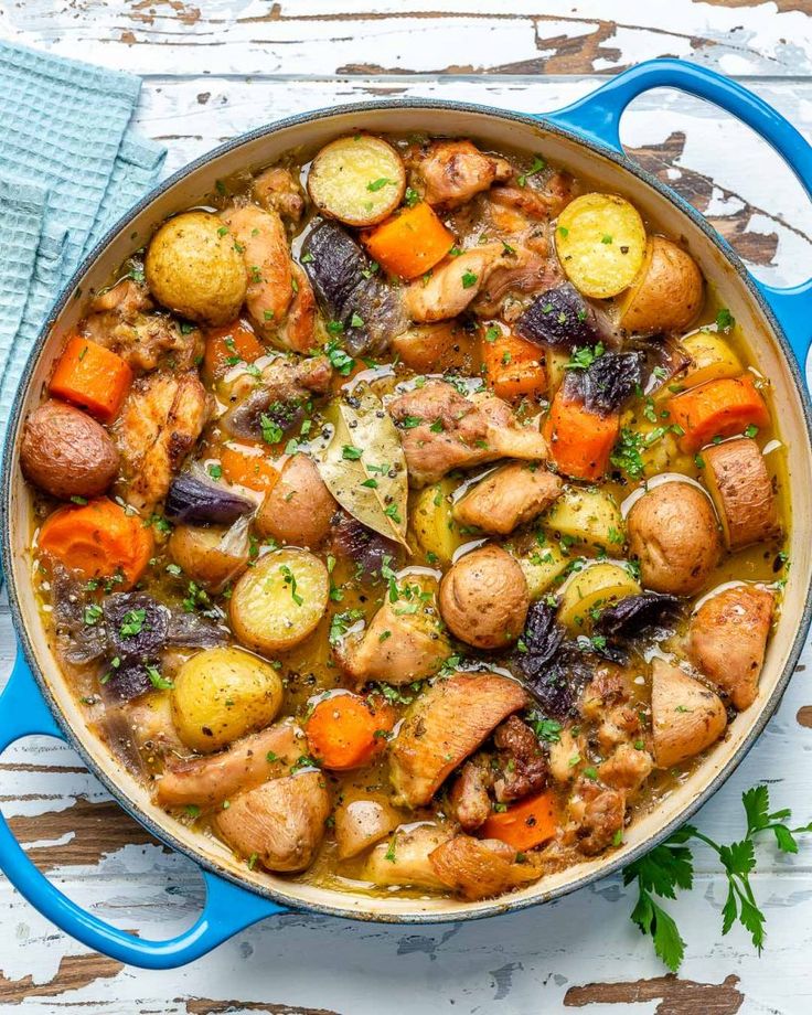 a blue pot filled with chicken, potatoes and carrots on top of a wooden table