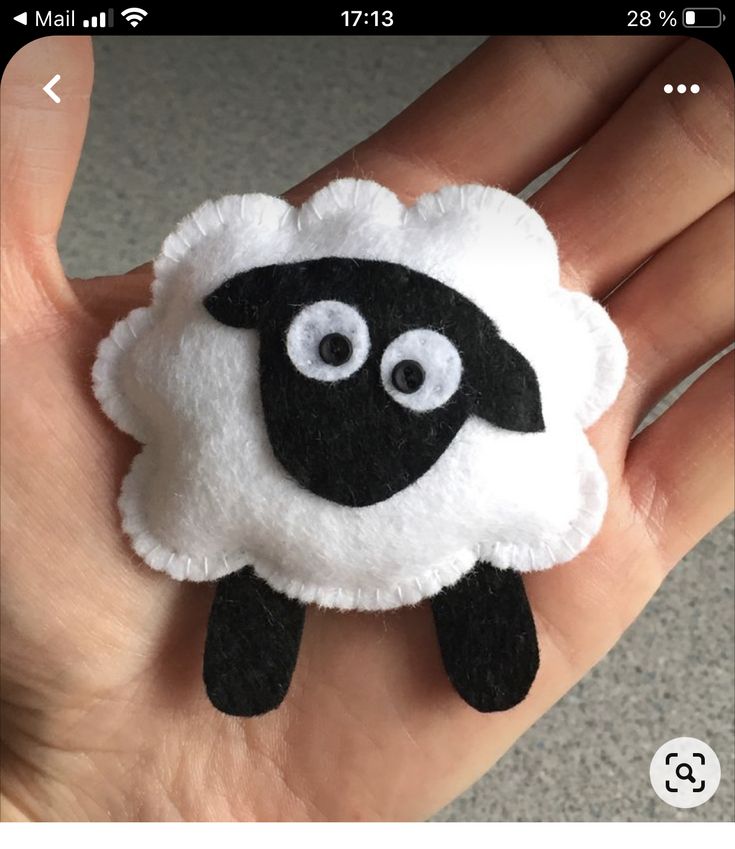 a hand holding a black and white sheep brooch