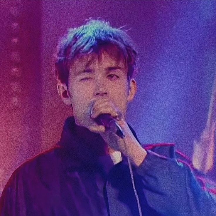 a man with blue hair singing into a microphone