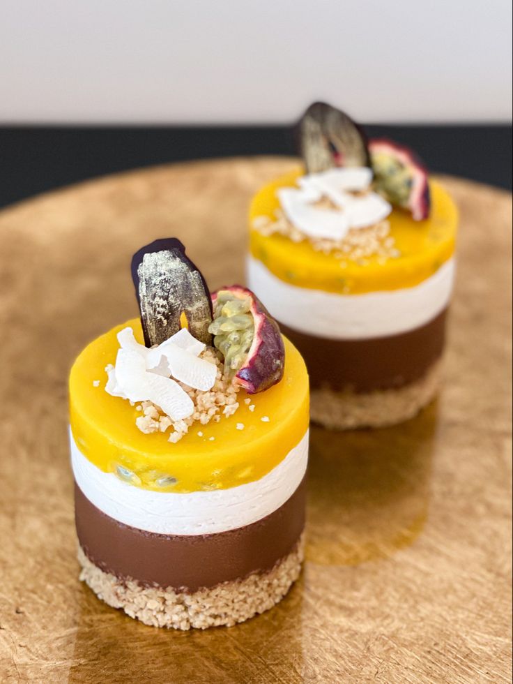 two desserts are sitting on top of a wooden plate, one is yellow and the other is brown