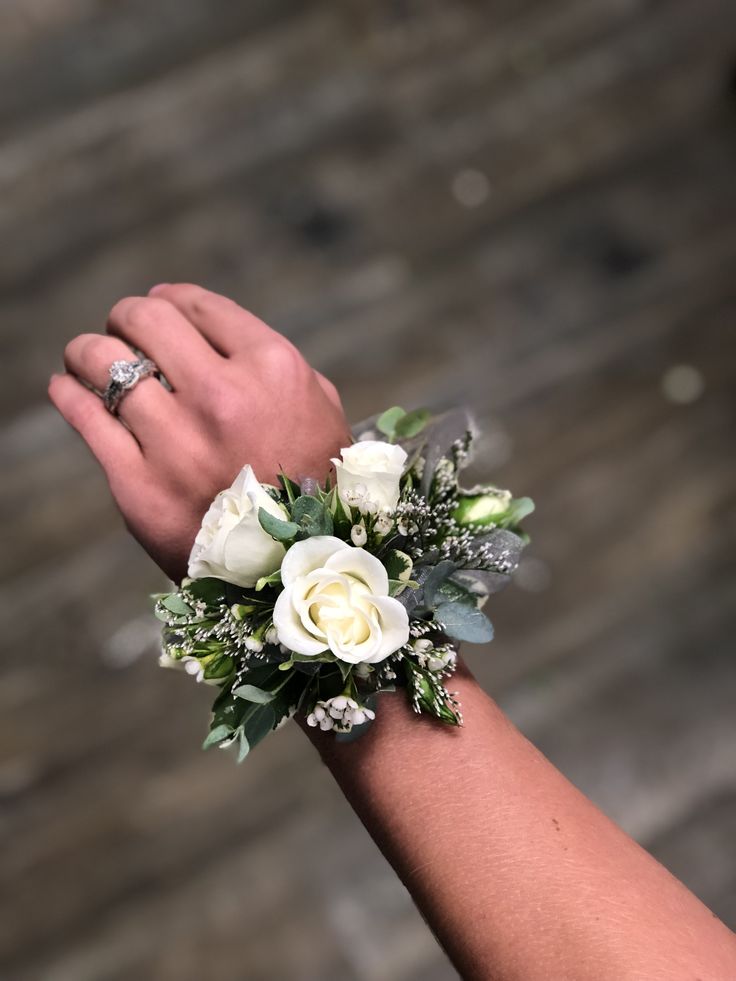 a woman's hand holding a white rose and greenery ring on her wrist