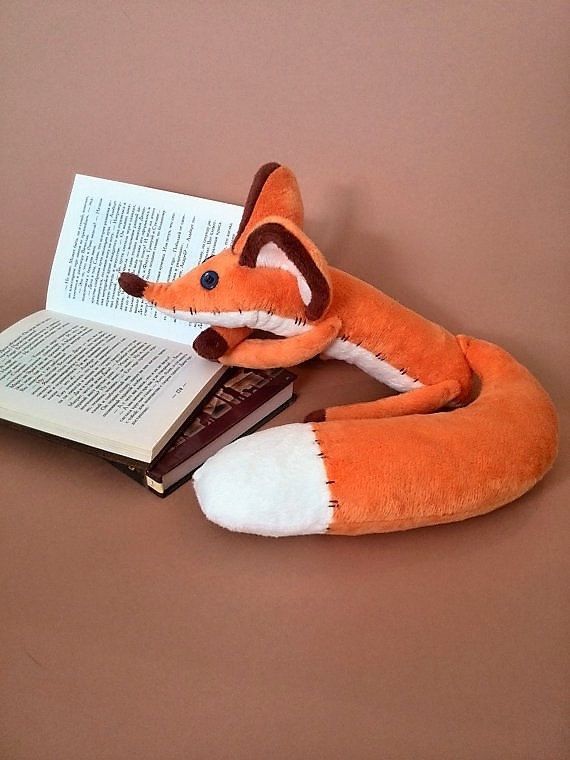 a stuffed fox reading a book on top of a table