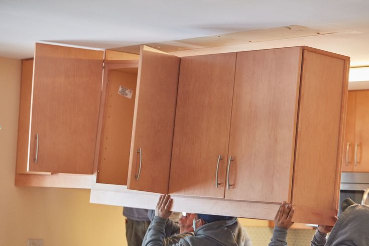 two people are hanging cabinets in the kitchen