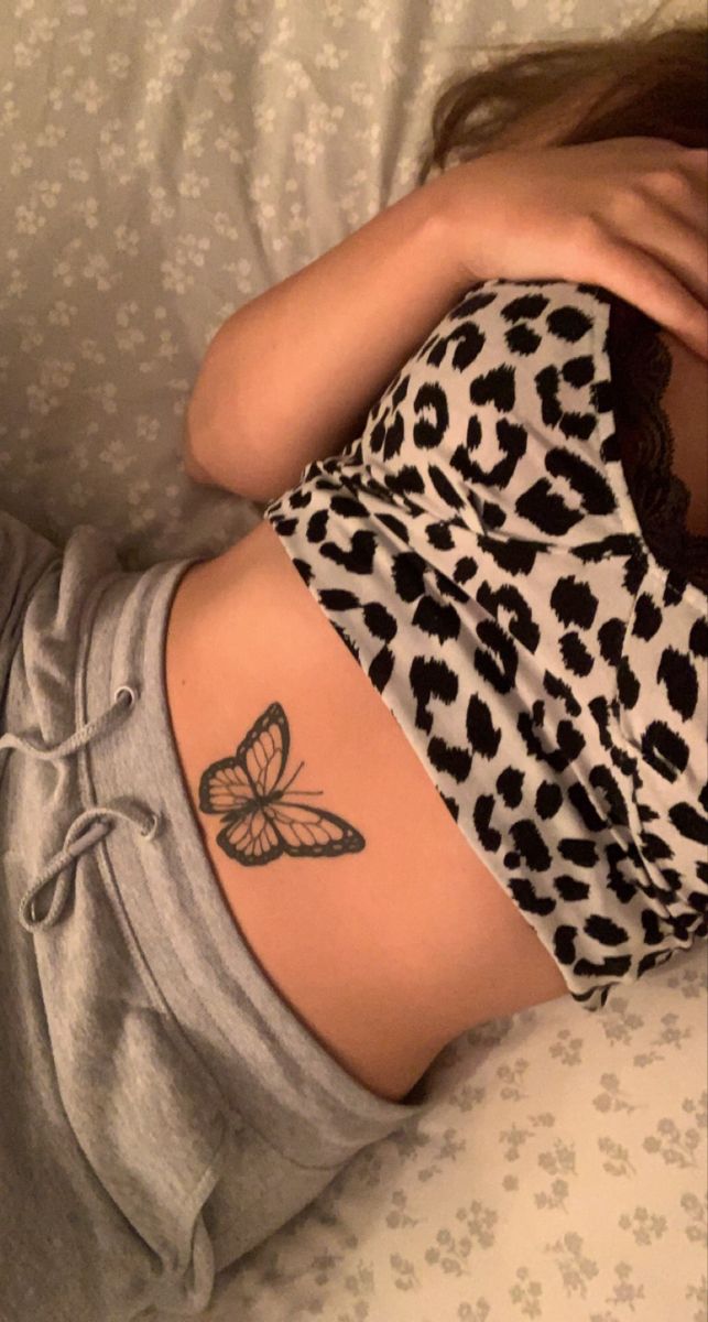 a woman with a butterfly tattoo on her back laying in bed next to a pillow