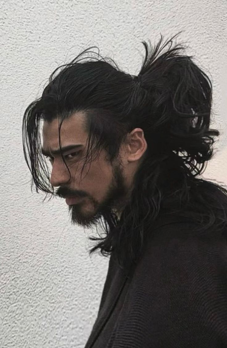 a man with long hair and a beard is standing in front of a white wall