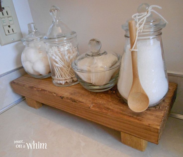 three glass jars with wooden spoons are on a wood shelf in front of the wall