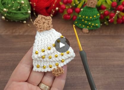 a hand holding a tiny crochet doll next to a knitting needle with christmas decorations in the background