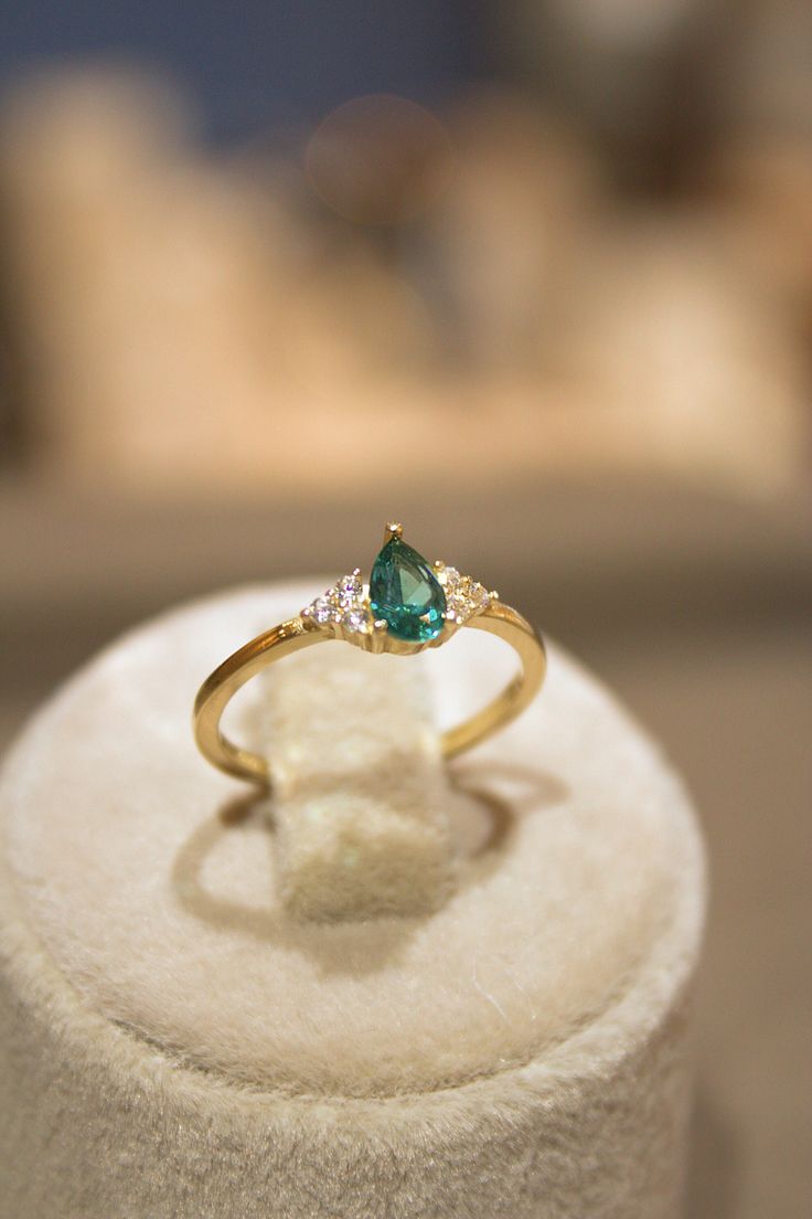 an engagement ring with a green stone and two white diamonds on it sitting on top of a display case