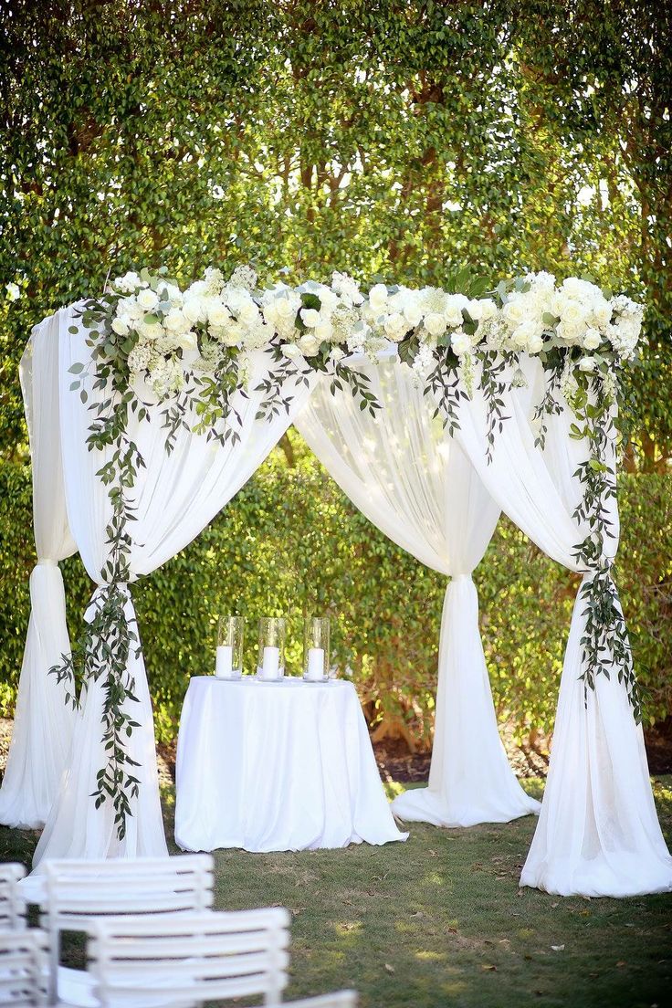 an outdoor wedding setup with white flowers and greenery on the top, draped drapes