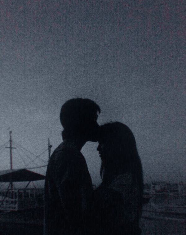 a man and woman kissing in the rain with an airplane flying overhead behind them on a cloudy day