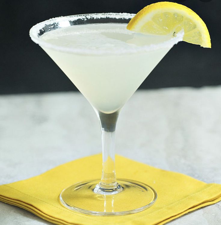 a white cocktail with a lemon slice on the rim in a martini glass next to a yellow napkin