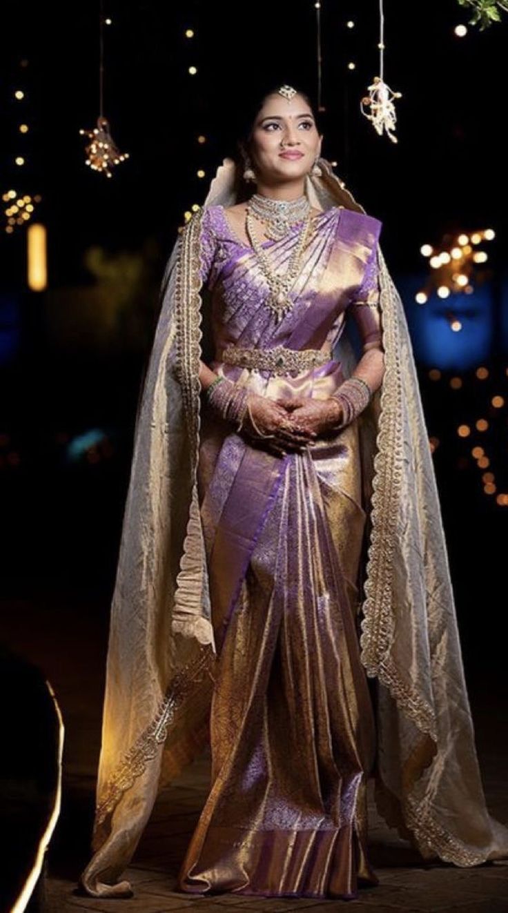 a woman in a purple and gold sari with lights hanging from the ceiling behind her