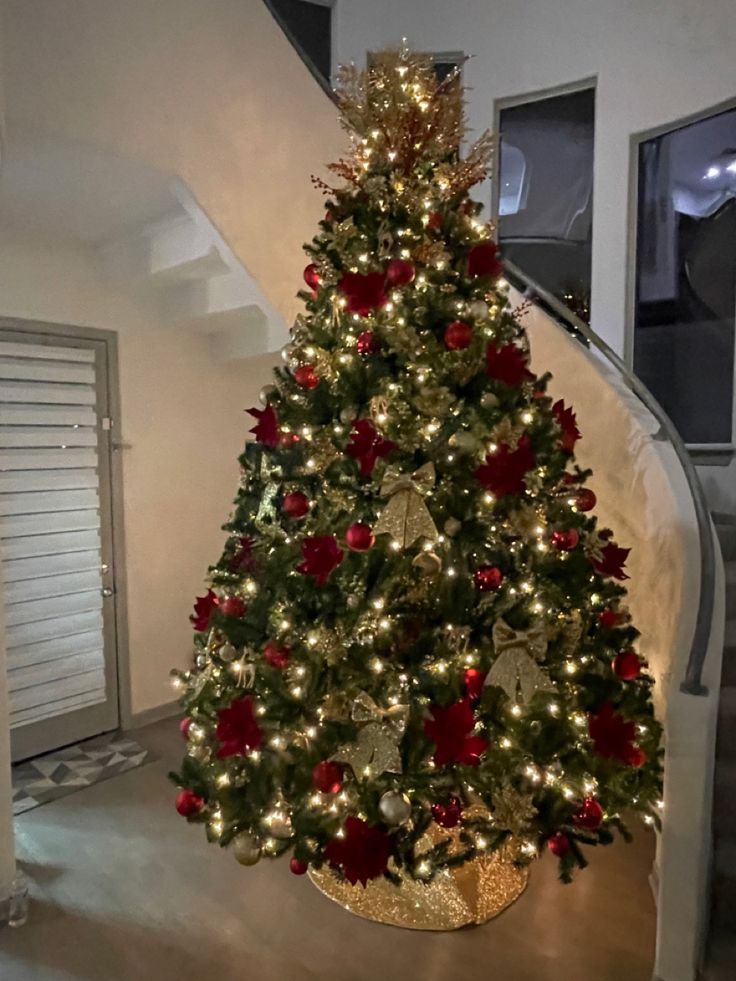 a decorated christmas tree with red and gold ornaments in a living room next to stairs