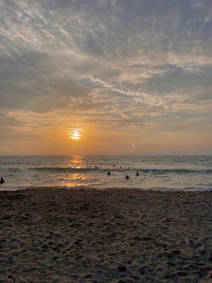 people are swimming in the ocean at sunset