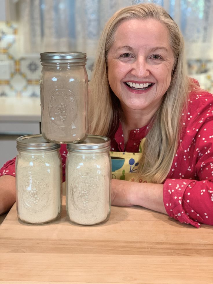 a woman sitting at a table with three jars in front of her and smiling for the camera