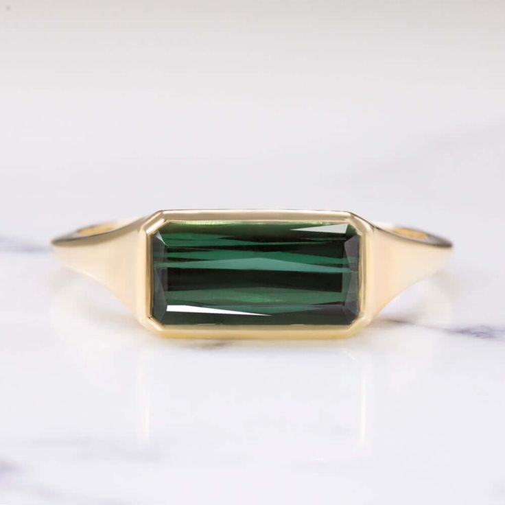 This beautiful and unique solitaire ring features a 1.72ct green tourmaline set in a sleek and elegant east west bezel setting! The tourmaline is a gorgeous forest green hue, and it has a beautiful play of light. The color is rich and luxurious, and it pairs perfectly with the yellow gold setting. The garnet’s emerald shape cut features angled facets in the pavilion similar to a criss cut. It’s a unique cutting style that creates a stunning play of light! The east west setting gives this classic Vintage Emerald Cut Ring, Elegant Backdrop, Half Bezel Setting, Antique Cushion, Handbags Vintage, Antique Engagement Rings Vintage, Ring Inspo, Emerald Cut Rings, Green Rings