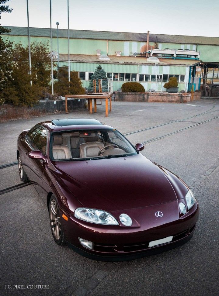 a maroon sports car is parked in front of a building with an empty parking lot