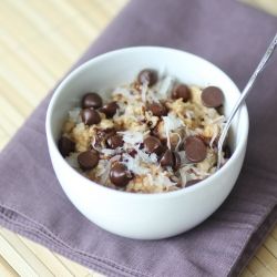 a white bowl filled with cereal and chocolate chips on top of a purple cloth next to a spoon