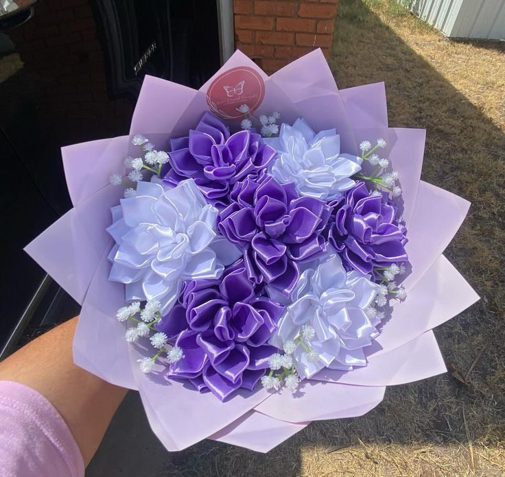 a bouquet of purple and white flowers is being held by someone's hand outside