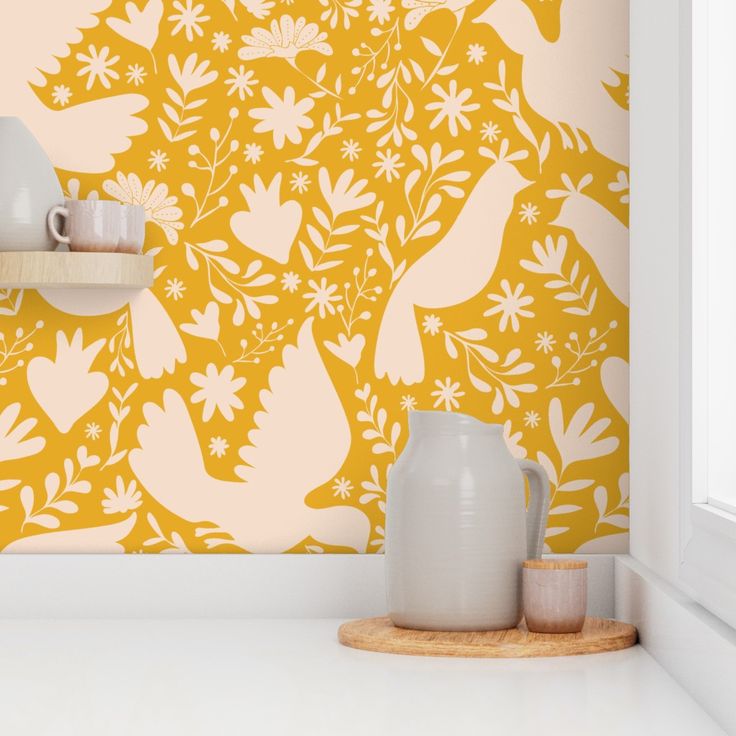 a yellow wall with white flowers and birds painted on it, next to two mugs