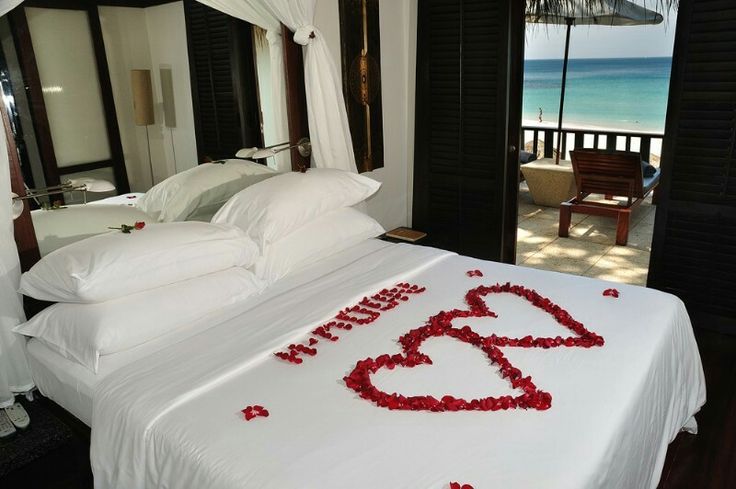 a bed with red rose petals on it in front of an open door to the beach