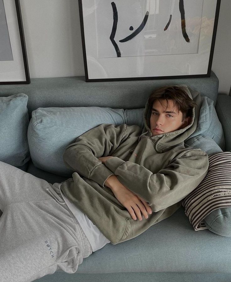 a young man laying on top of a blue couch next to two framed pictures above him