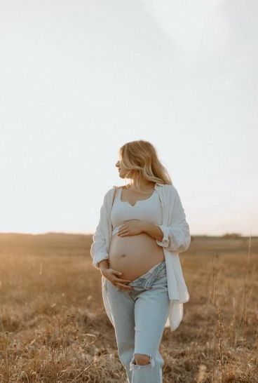 a pregnant woman walking through a field with her belly in the air while wearing ripped jeans