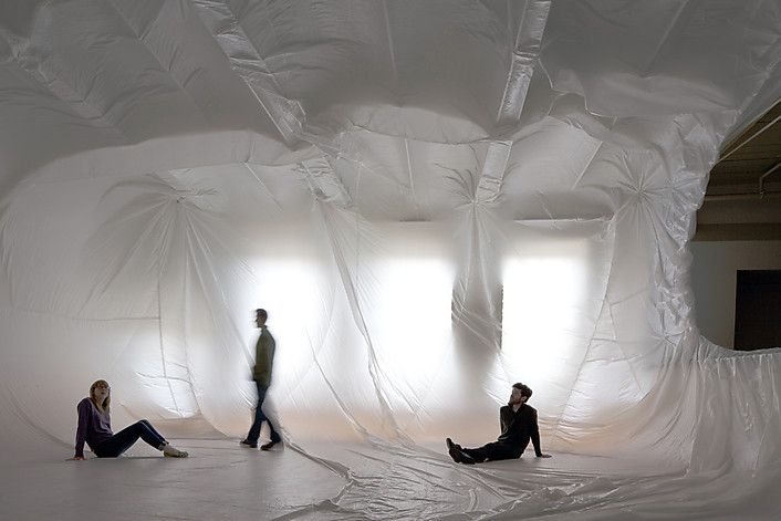 three people sitting on the ground in a room with white walls and sheets covering them