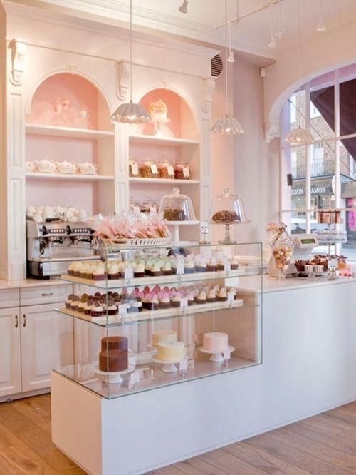 a bakery filled with lots of cakes and cupcakes on top of glass shelves