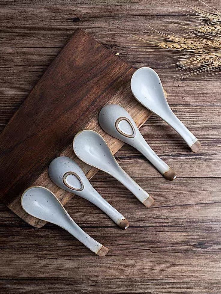 four spoons are lined up on a cutting board next to some ears of wheat