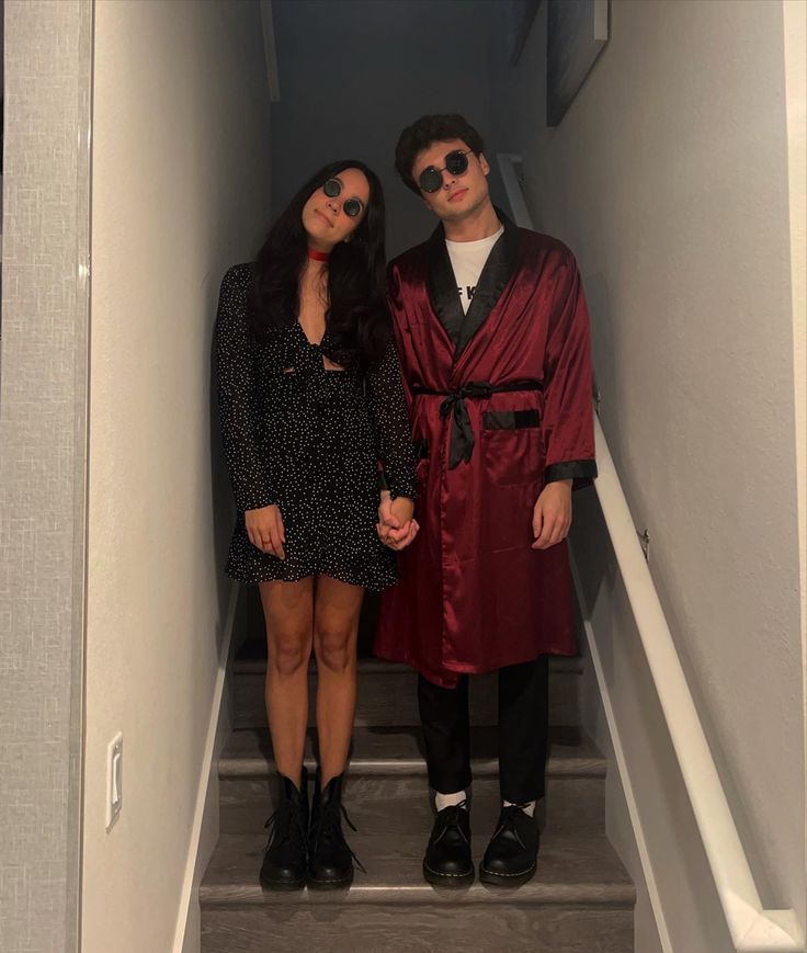 a man and woman standing on the stairs in front of an open door wearing red robes