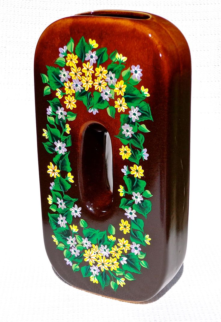 a brown vase with yellow and white flowers painted on the front, sitting against a white background