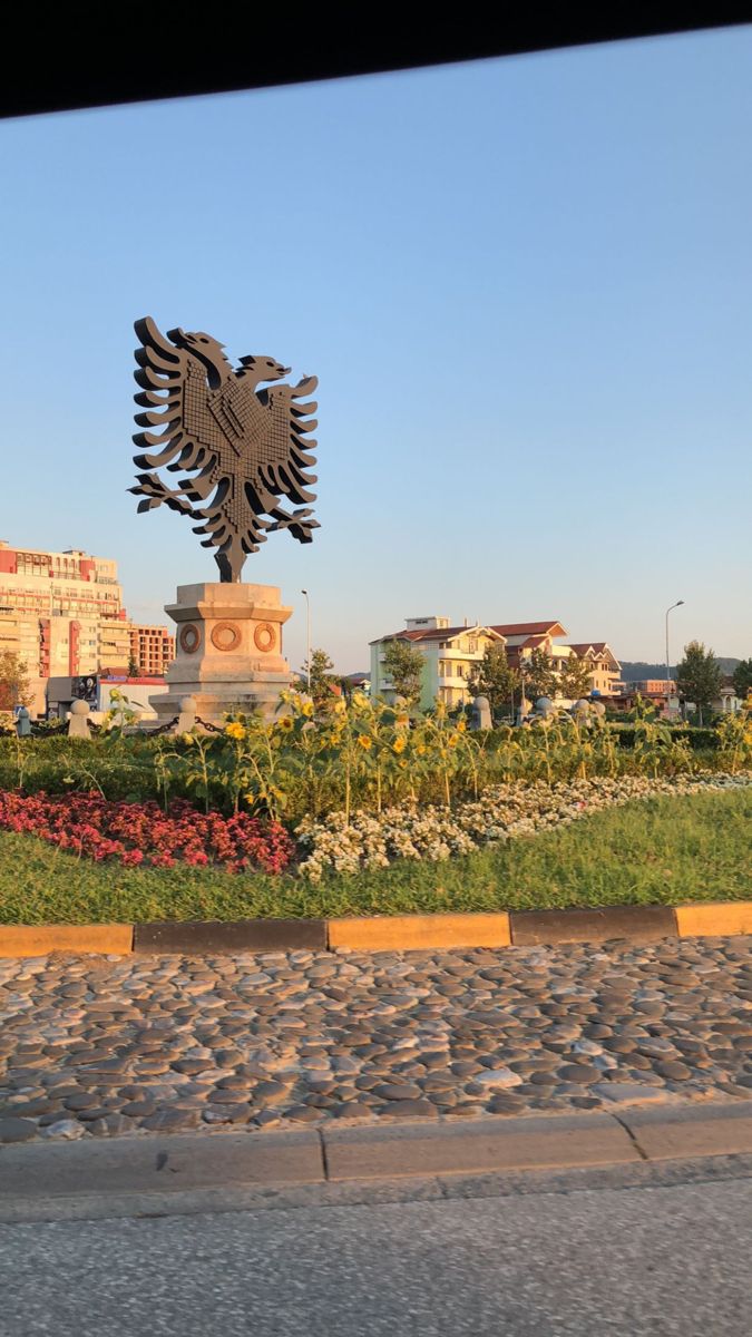 a large metal eagle sitting on top of a lush green field next to a park