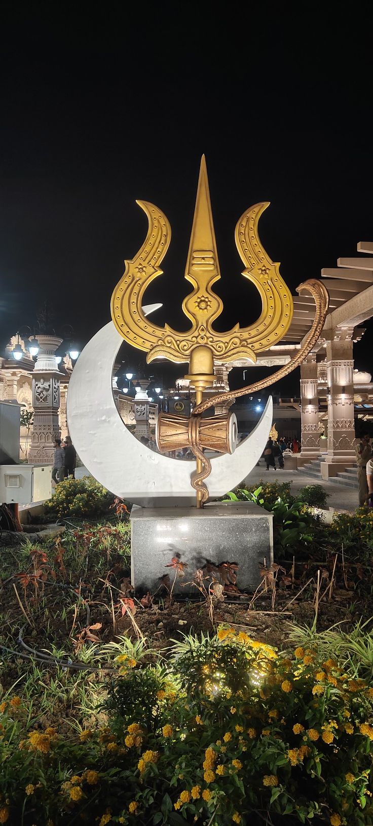 a large gold and white clock sitting in the middle of a park at night time