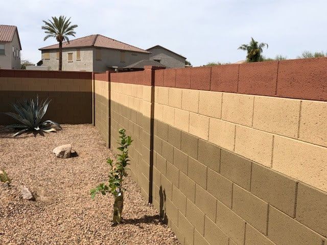 a fenced in area with rocks and plants next to the wall that is made out of concrete