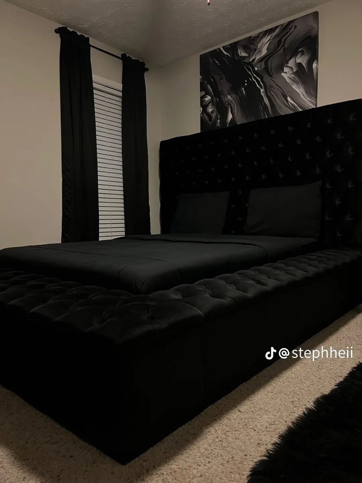 a bed with black sheets and pillows in a room next to a painting on the wall