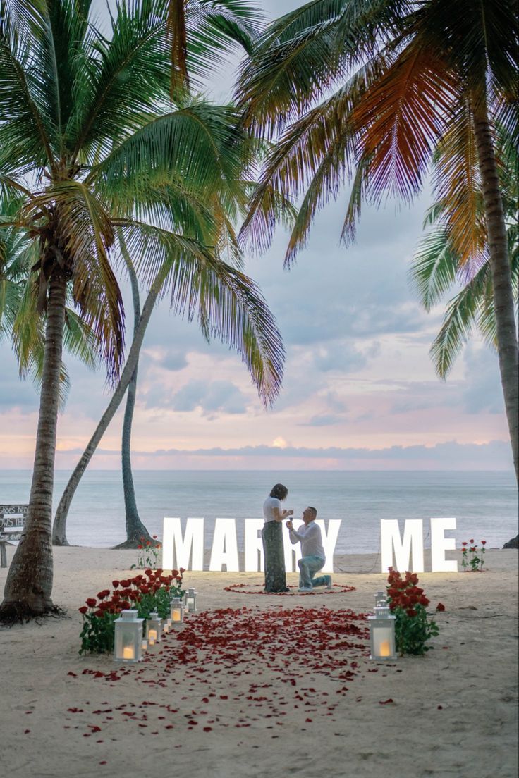 two people standing under palm trees with the word marry me written in front of them