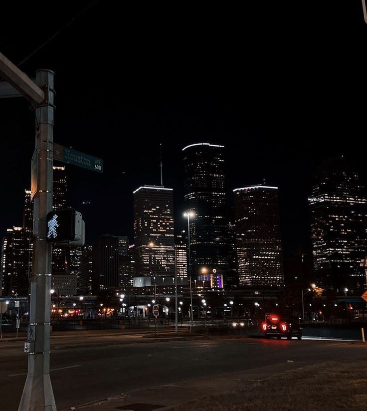 the city skyline is lit up at night, with street signs and traffic lights in foreground