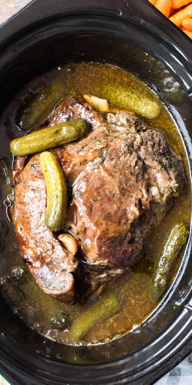 a close up of food in a crock pot with carrots and pickles