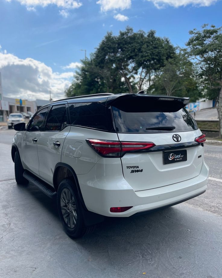 the rear end of a white toyota highland parked in a parking lot next to trees